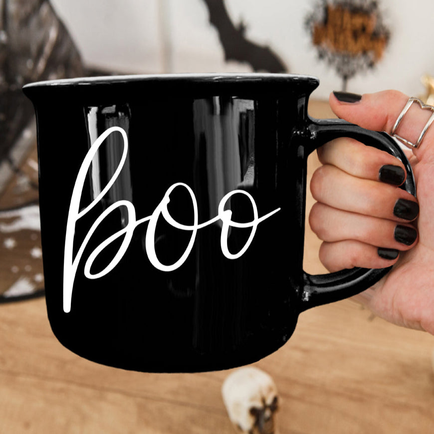 Black mug with 'boo' written on it held by a person.