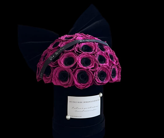 Bouquet of pink and black roses in a black box with a decorative bow on a reflective surface.