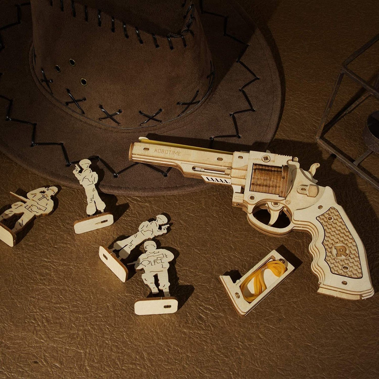 Wooden toy gun and figures on a brown leather surface with a cowboy hat.