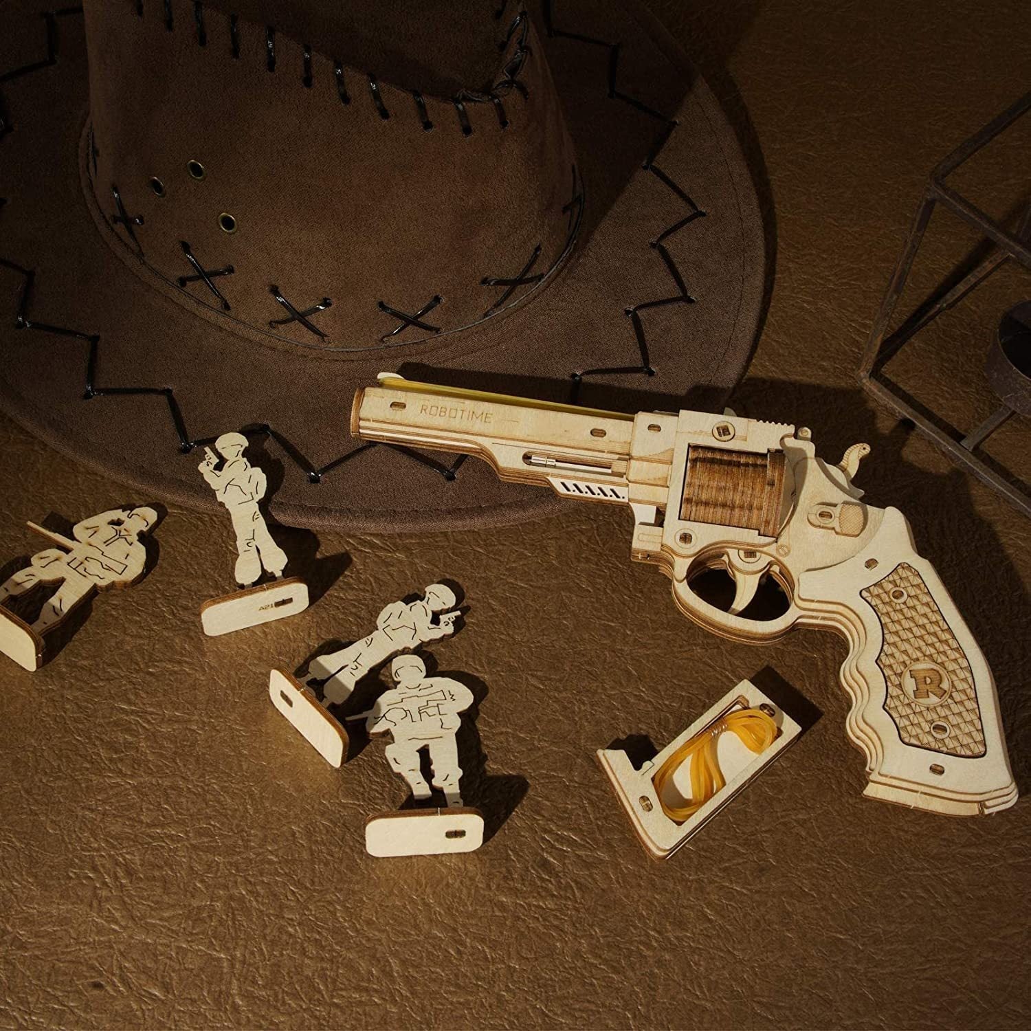 Wooden toy gun and figures on a brown leather surface with a cowboy hat.