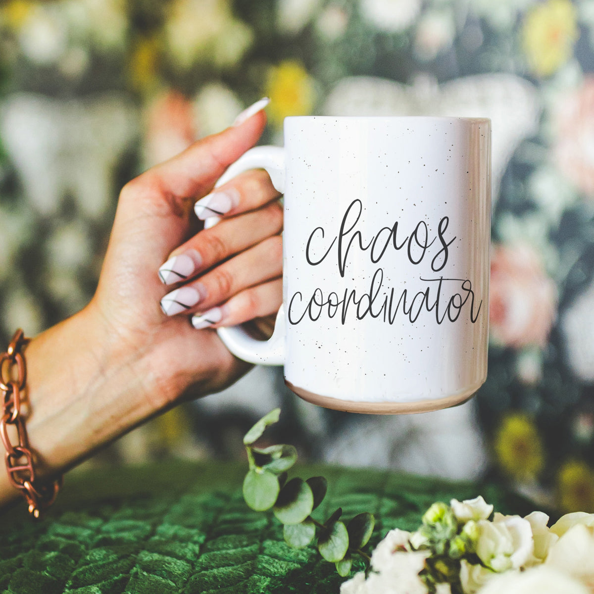 Hand holding a mug with 'chaos coordinator' text against a blurred natural background