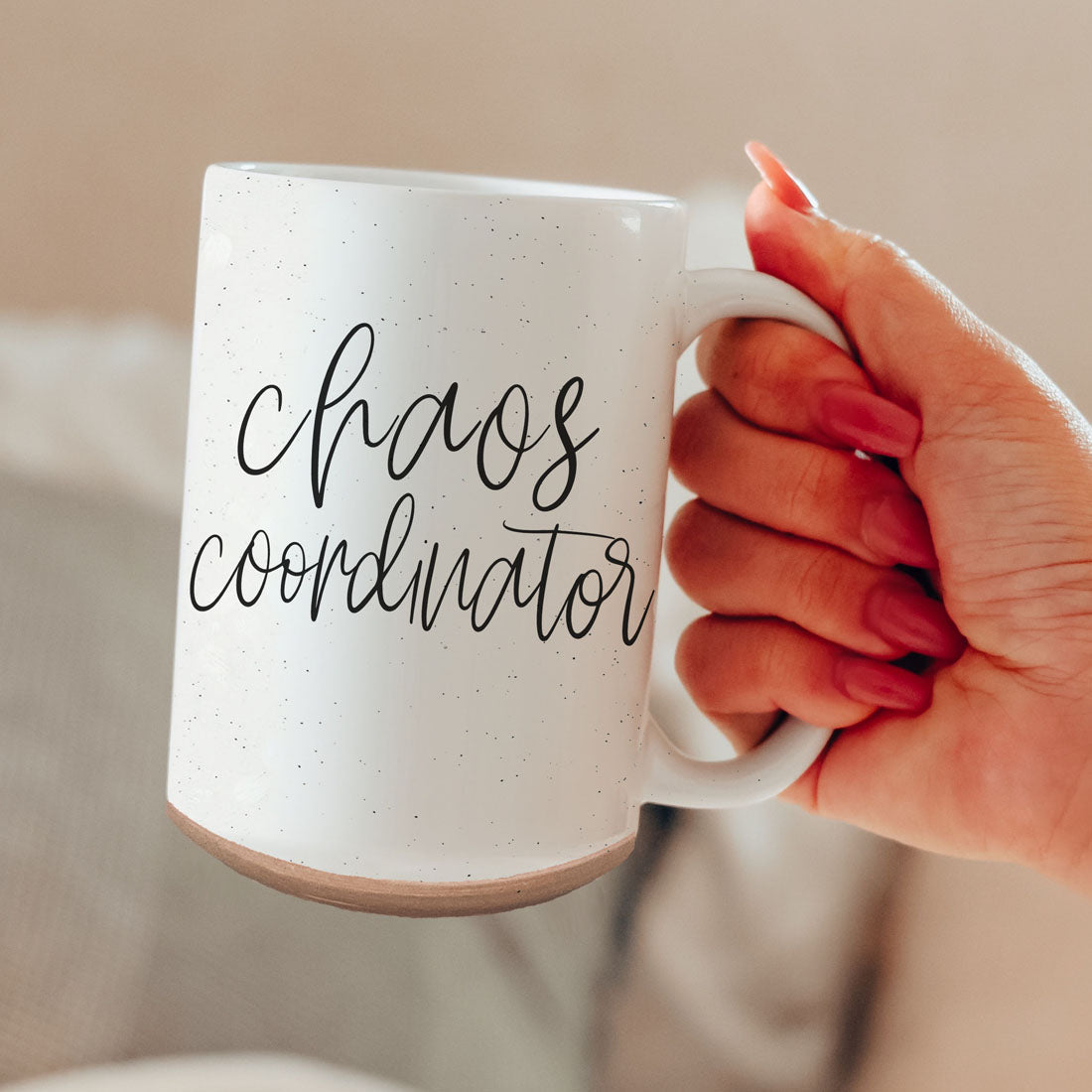 White mug with 'chaos coordinator' text held by a hand against a neutral background