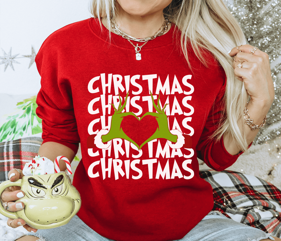 Person wearing a red 'Christmas' sweater holding a Grinch mug.