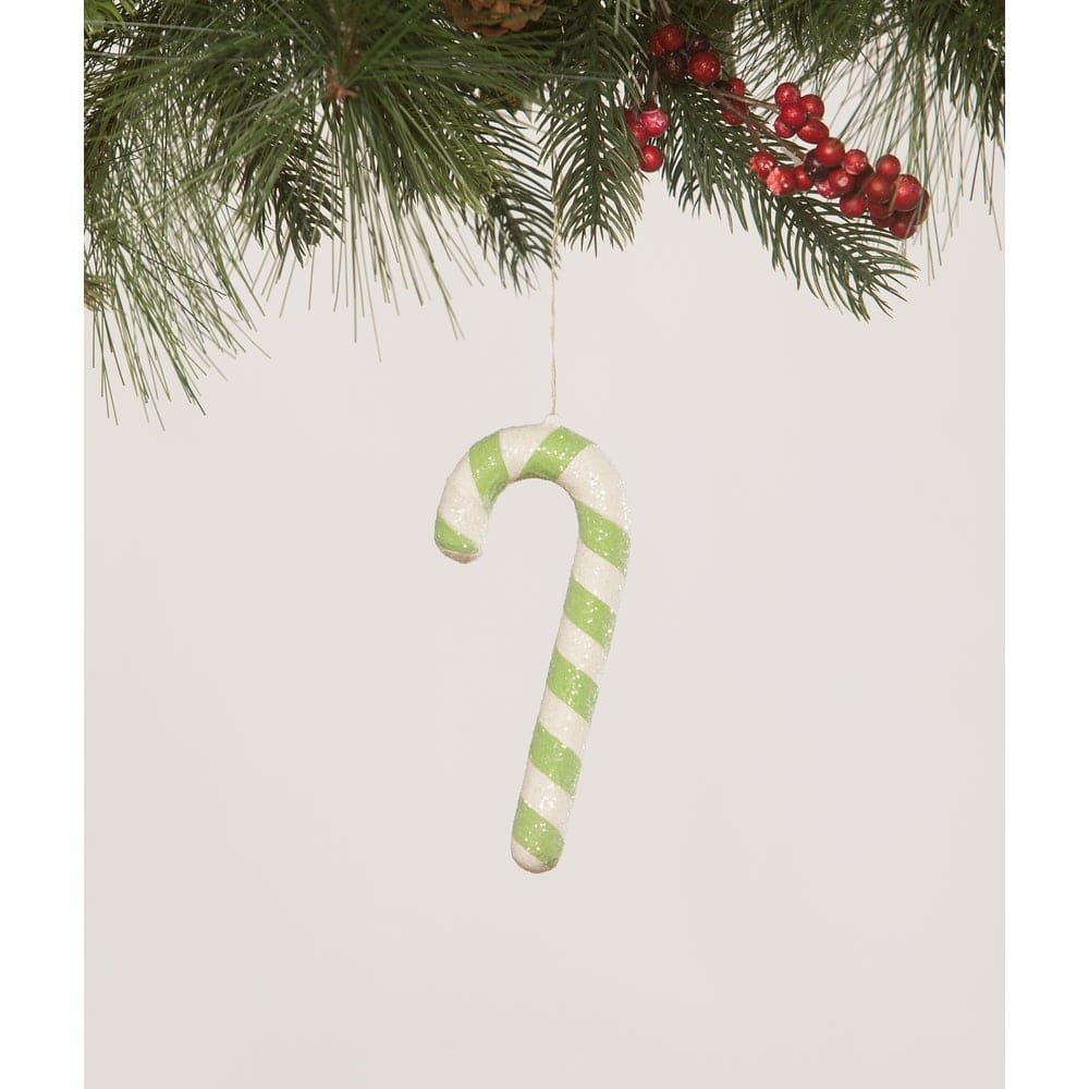 Green and white striped candy cane ornament hanging from a branch with red berries on a light gray background