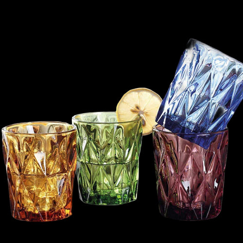 Set of three colorful glass tumblers with a lemon slice and blue ice cube on a white background