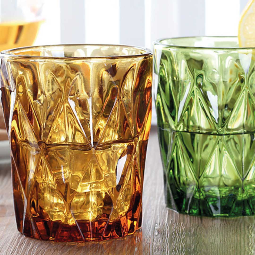 Two patterned glass tumblers, one amber and one green, on a light surface.