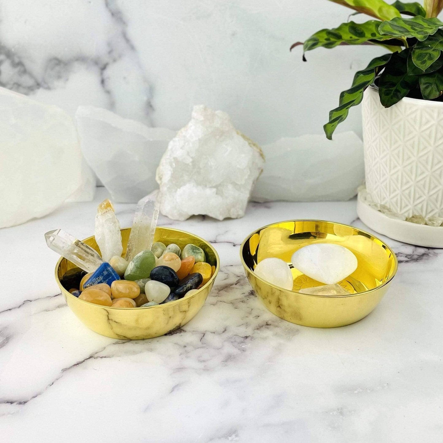 Two gold bowls on a marble surface with crystals and stones.