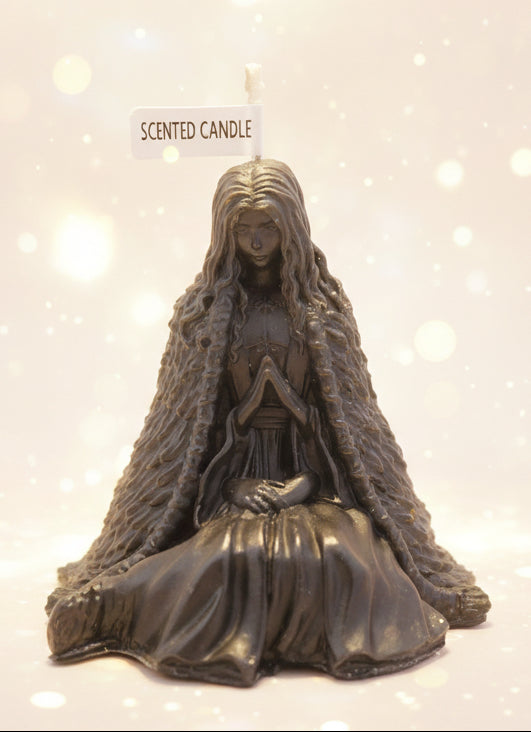 Dark-colored figurine of a hooded figure with a 'Scented Candle' label on a surface with books in the background.