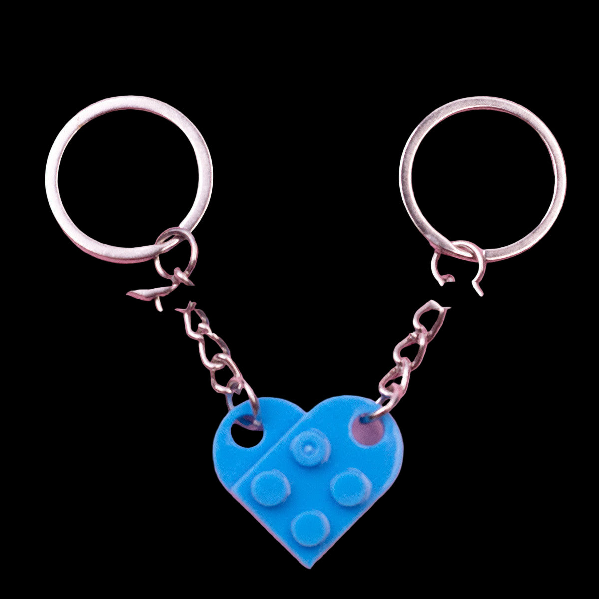 Two keychains with a blue heart-shaped LEGO piece on a pink background