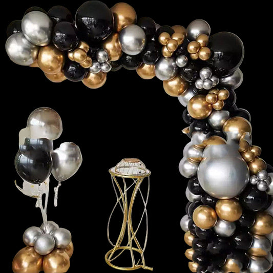 Balloon arch with black, gold, and silver balloons in a room with a decorative table.