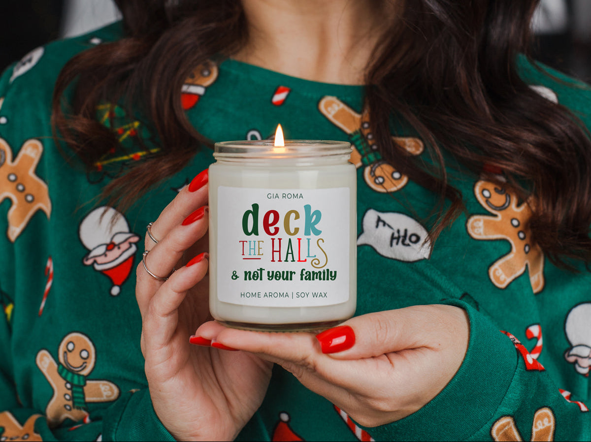 Person wearing a festive sweater holding a lit candle labeled 'deck the halls & not your family'.