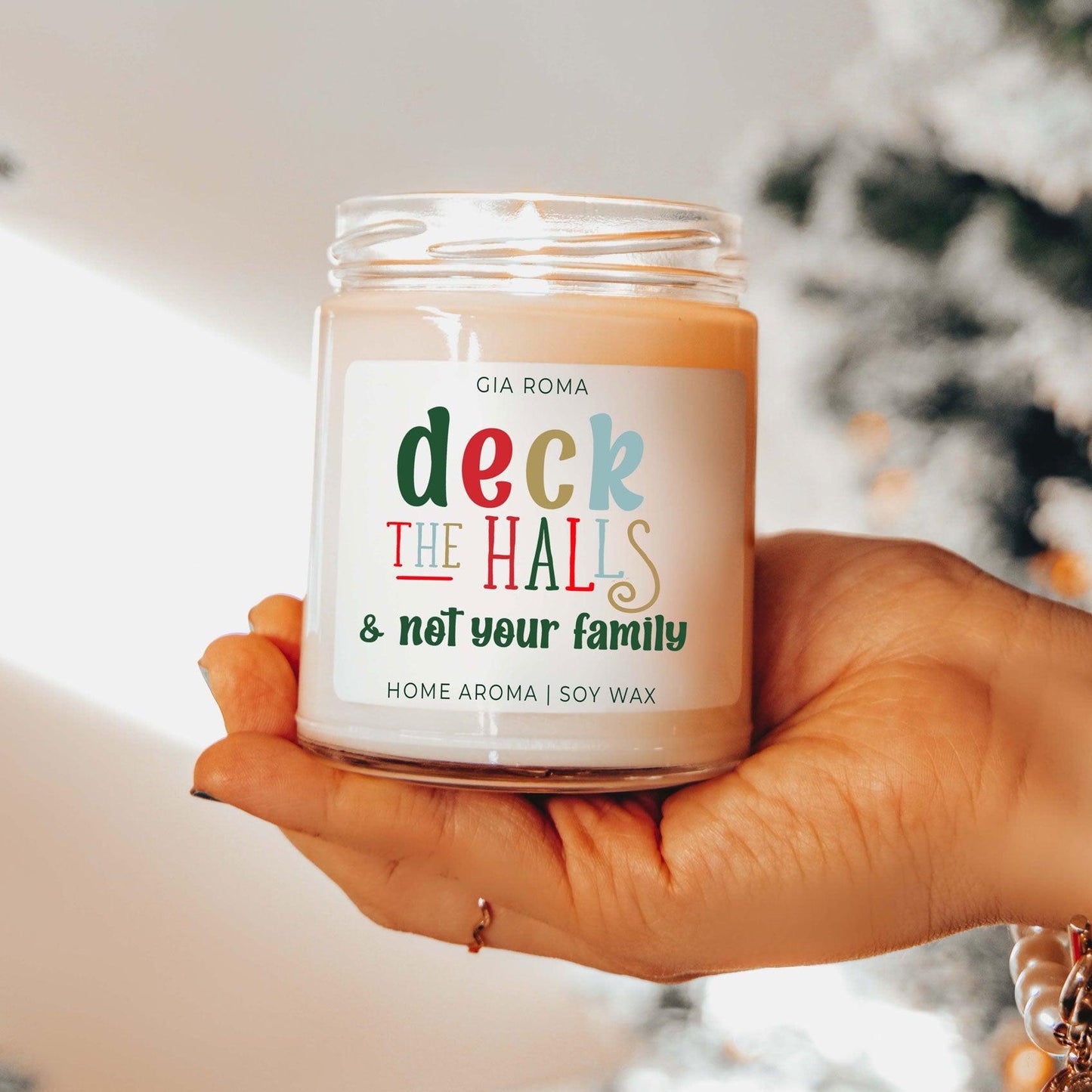 Hand holding a candle labeled 'deck the halls & not your family' with a blurred background