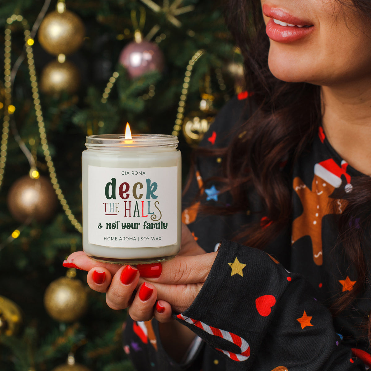 Person holding a candle labeled 'deck the halls and not your family' in front of a decorated Christmas tree.