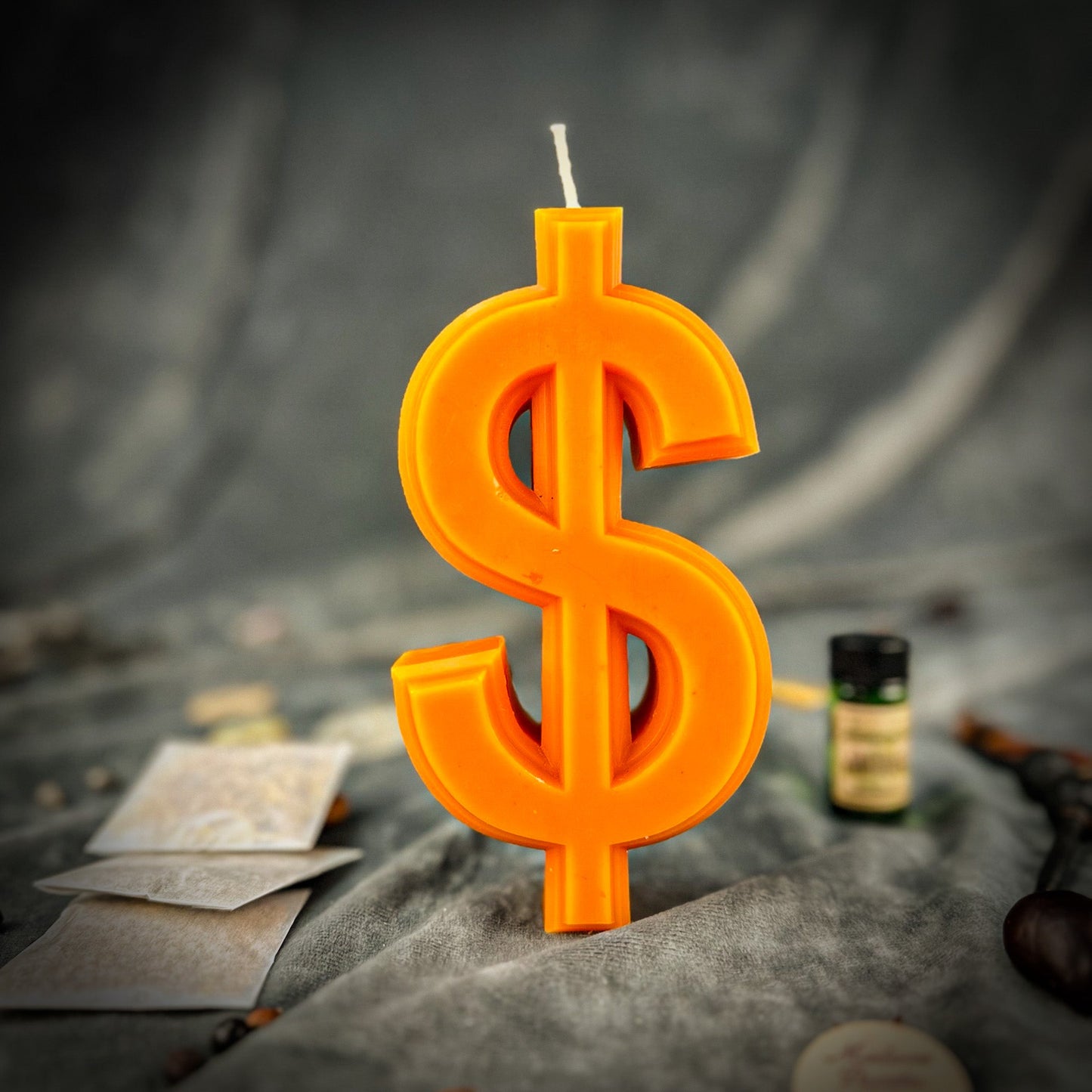 Orange dollar sign candle on a dark surface with coins and a bottle in the background