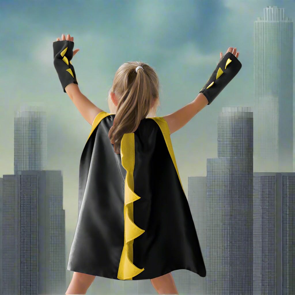Child wearing a superhero cape and gloves on a wooden deck.
