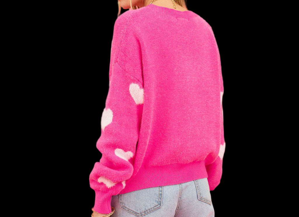 Person wearing a pink sweater with white polka dots and light blue jeans against a pink background