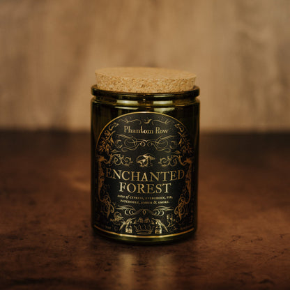 Candle jar labeled 'Enchanted Forest' by Phantom Row on a wooden surface with a blurred background.