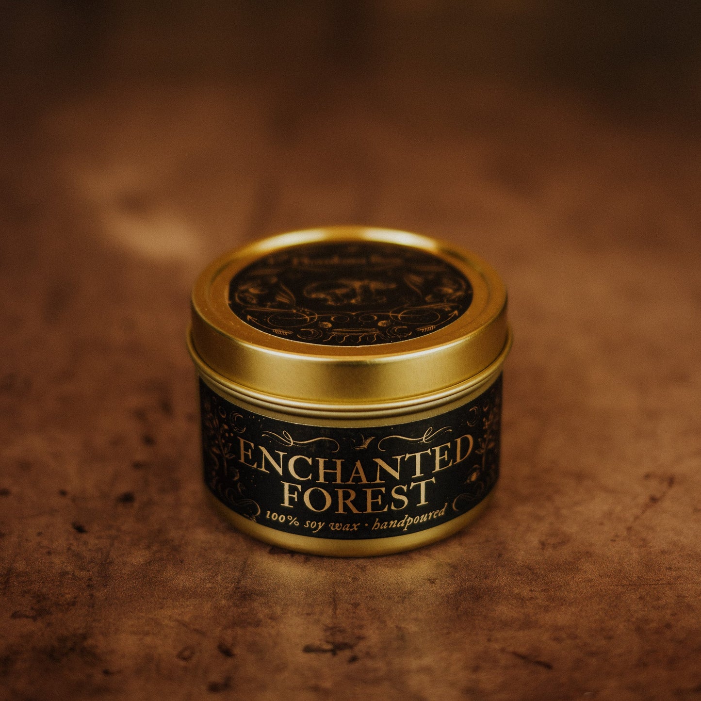 Candle jar labeled 'Enchanted Forest' with a gold lid on a textured brown background
