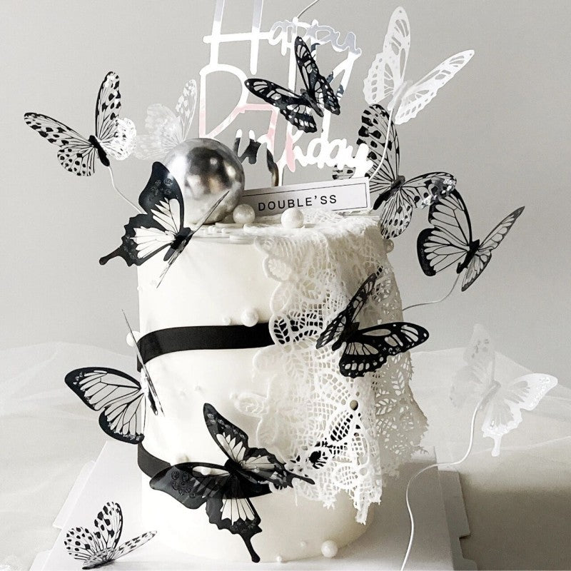 White cake with black butterflies and 'Happy Birthday' topper on a light gray background