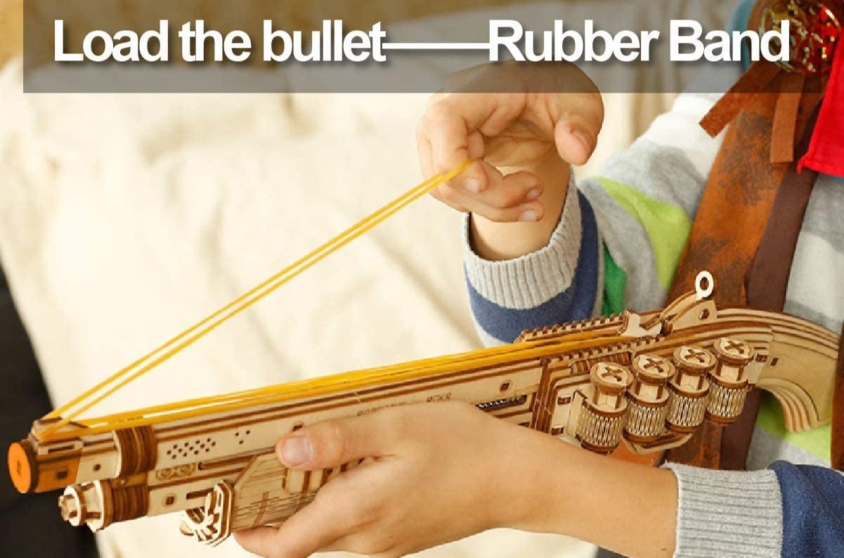 Wooden toy crossbow with rubber band and text 'Load the bullet —— Rubber Band' on a blurred background.