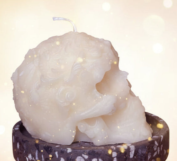 White skull-shaped candle on a black terrazzo holder against a textured gray background