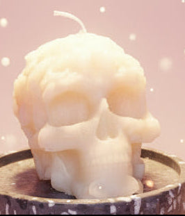 Skull-shaped candle on a black holder against a textured gray background