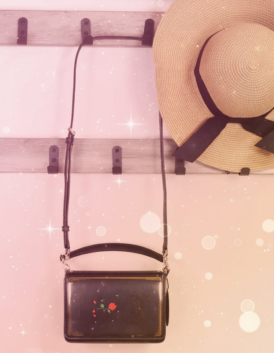 Black handbag with red and white design hanging on a wooden rack with a straw hat above it, branded 'Handmethebag'.