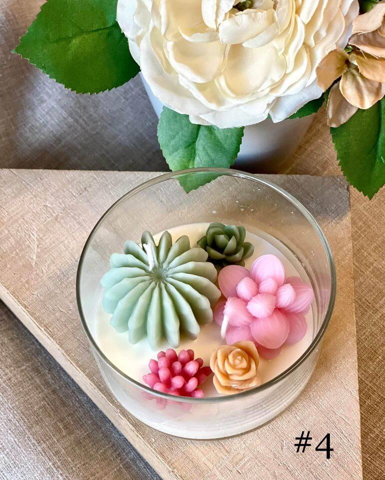 Decorative candle with colorful succulent-shaped wax melts on a wooden surface with flowers in the background.