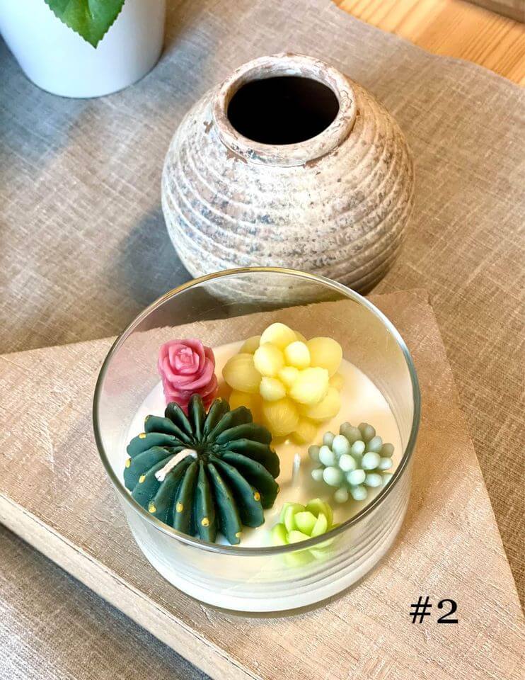 Glass container with decorative succulent-shaped candles on a wooden surface