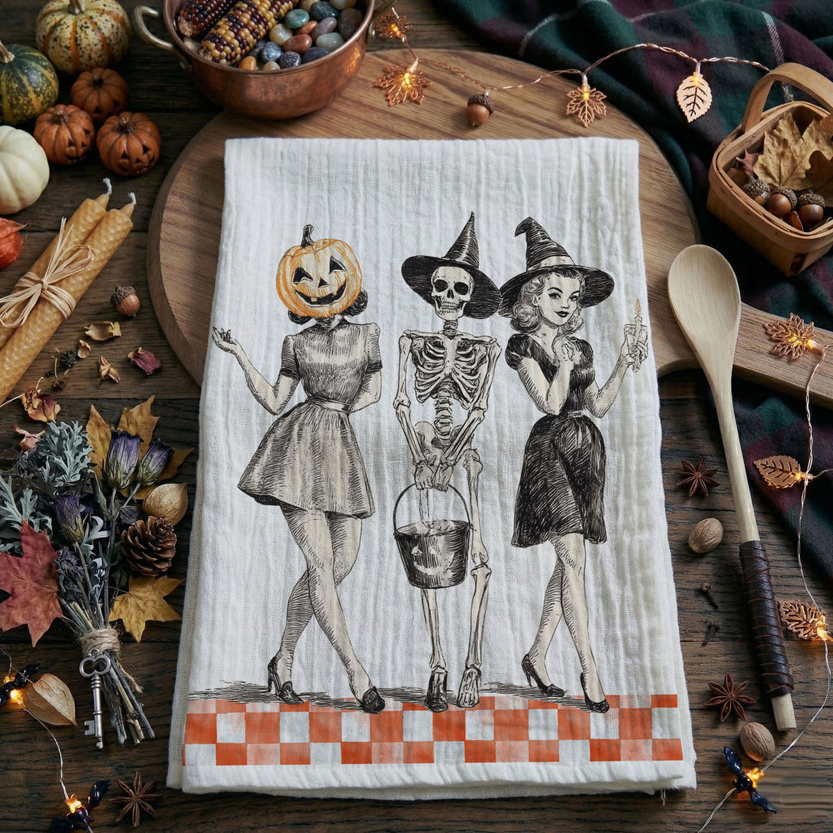 Halloween-themed kitchen towel with skeletons and pumpkins on a wooden table with autumn decorations.