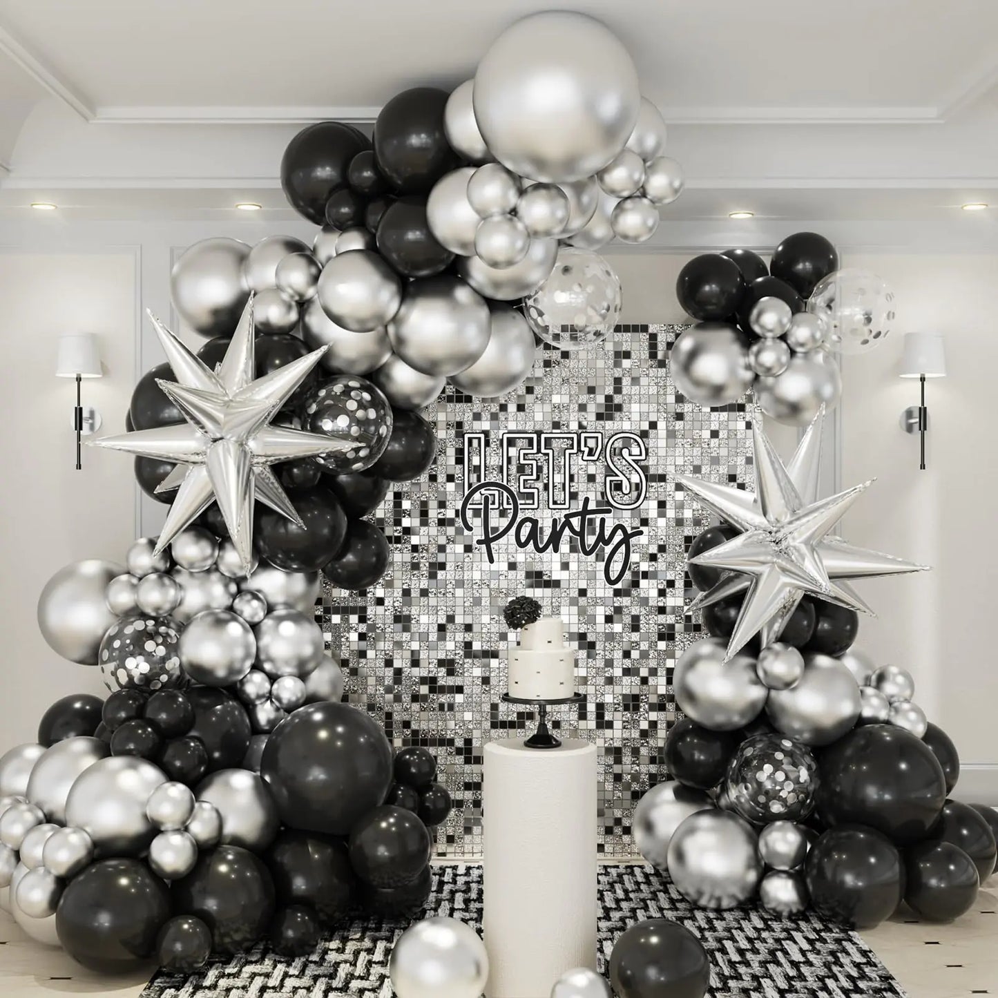Black, silver, and white balloon arch with 'Let's Party' sign in a room with decorative wall.