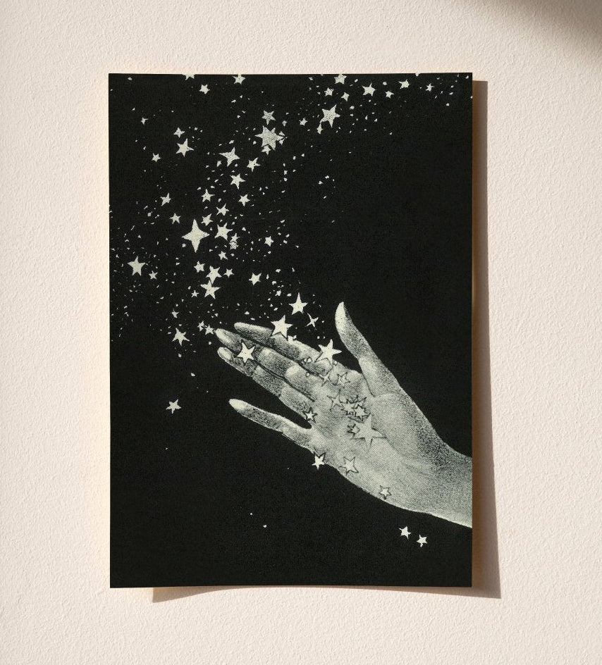Greeting card with a hand holding stars against a black background on a beige surface