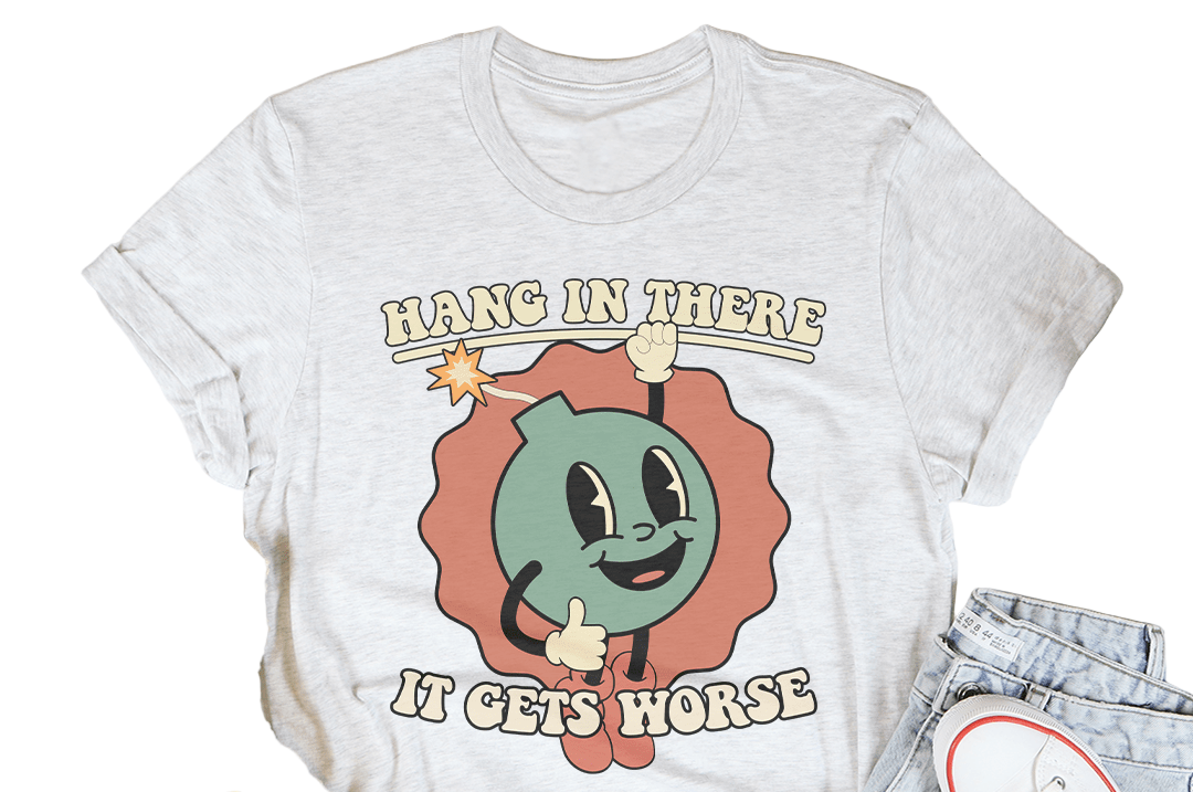 White t-shirt with cartoon character and text 'Hang in there, it gets horse' on a white background with casual items.