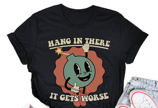Black t-shirt with cartoon design and text 'Hang in there it gets worse' on a white surface with casual items.