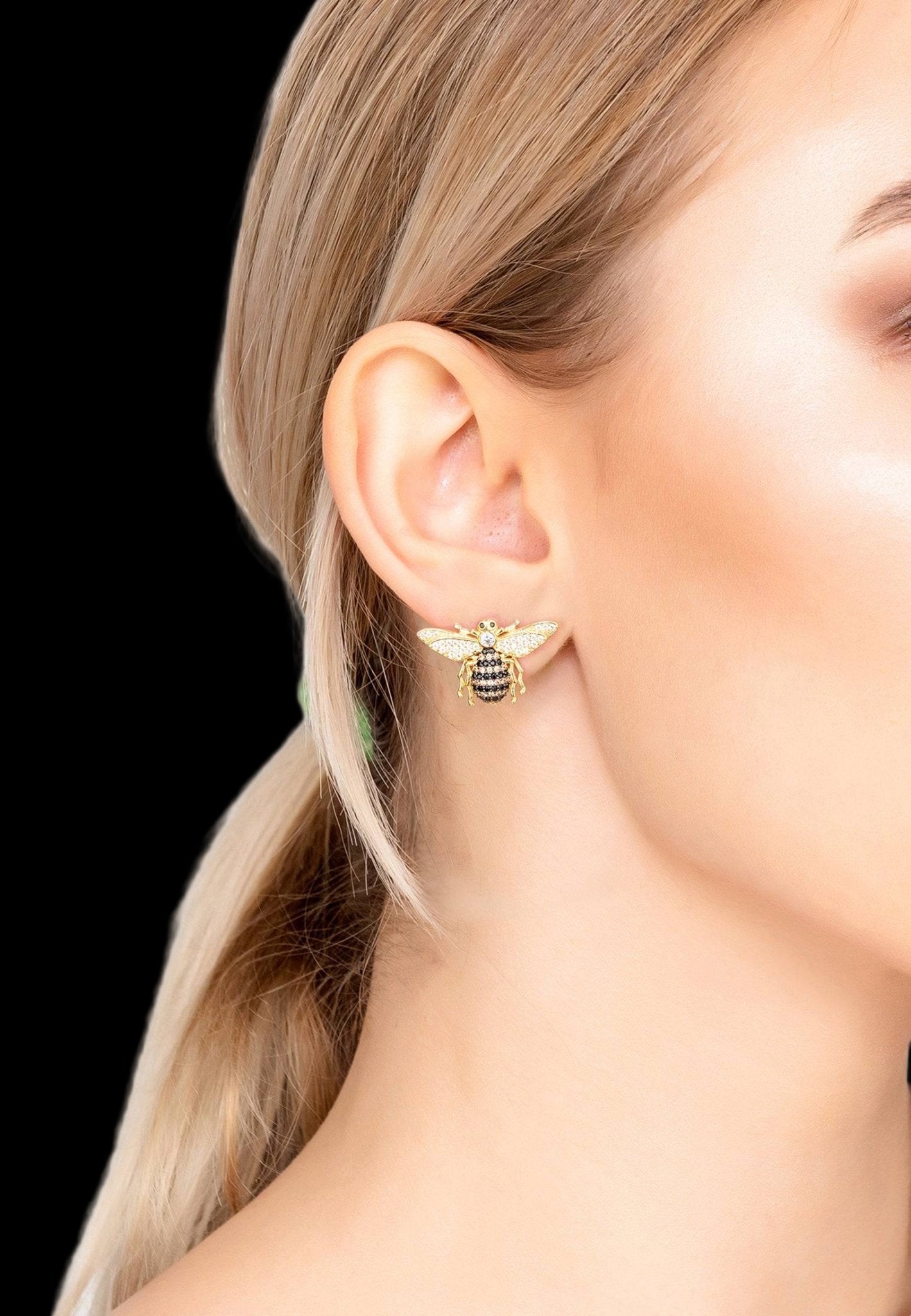 Gold bee-shaped earrings worn by a person with blonde hair.