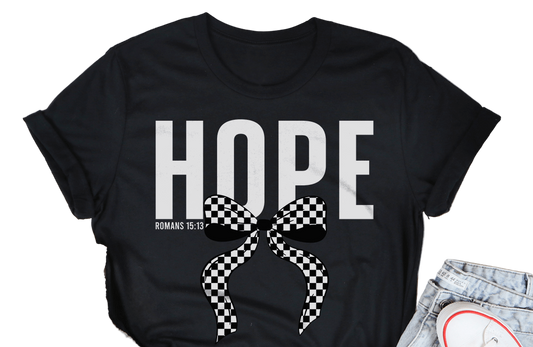 Black t-shirt with 'HOPE' and a bow graphic on a wooden surface with casual items.