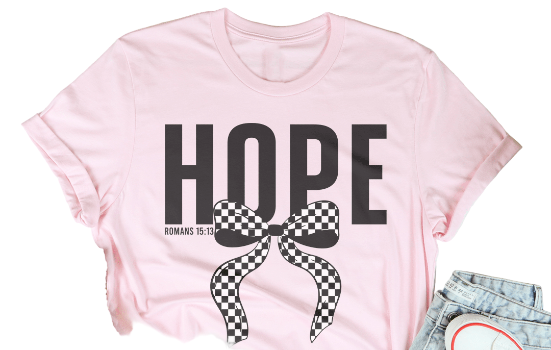 Pink t-shirt with 'HOPE' and a bow graphic, surrounded by casual items on a light wooden surface.