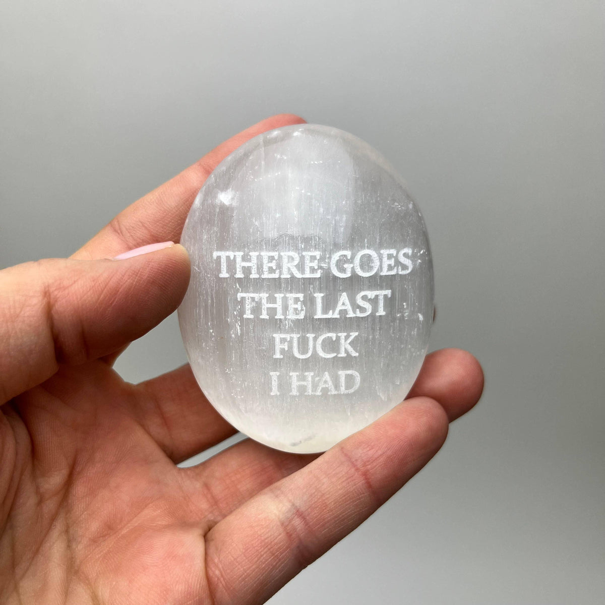Hand holding a crystal with engraved text against a gray background