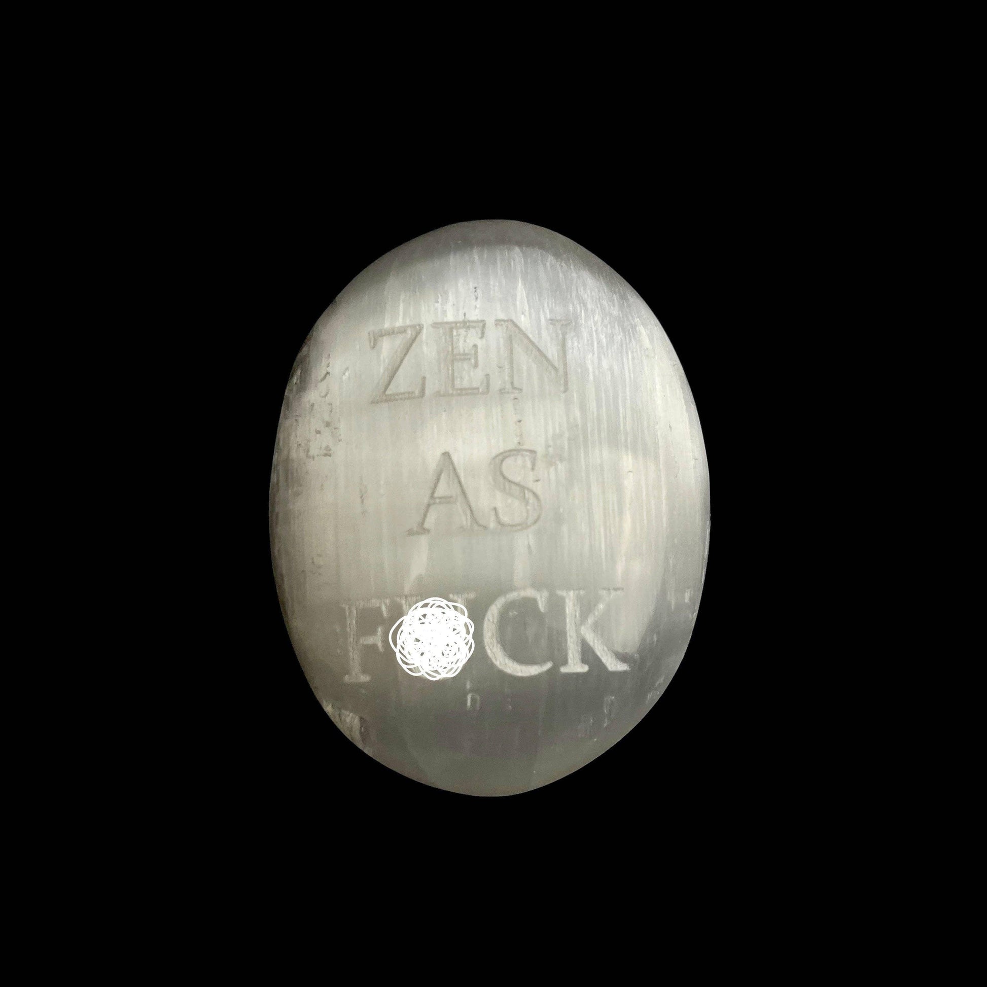 A polished silver oval stone or medallion engraved with the text 'ZEN AS F*CK' and a small circular floral detail, shown against a solid black background.