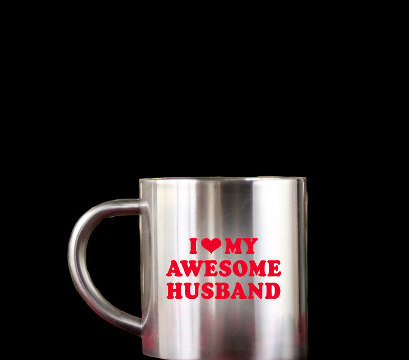 Silver mug with 'I ❤️ MY AWESOME HUSBAND' text on a red checkered tablecloth with a blurred Christmas tree background.