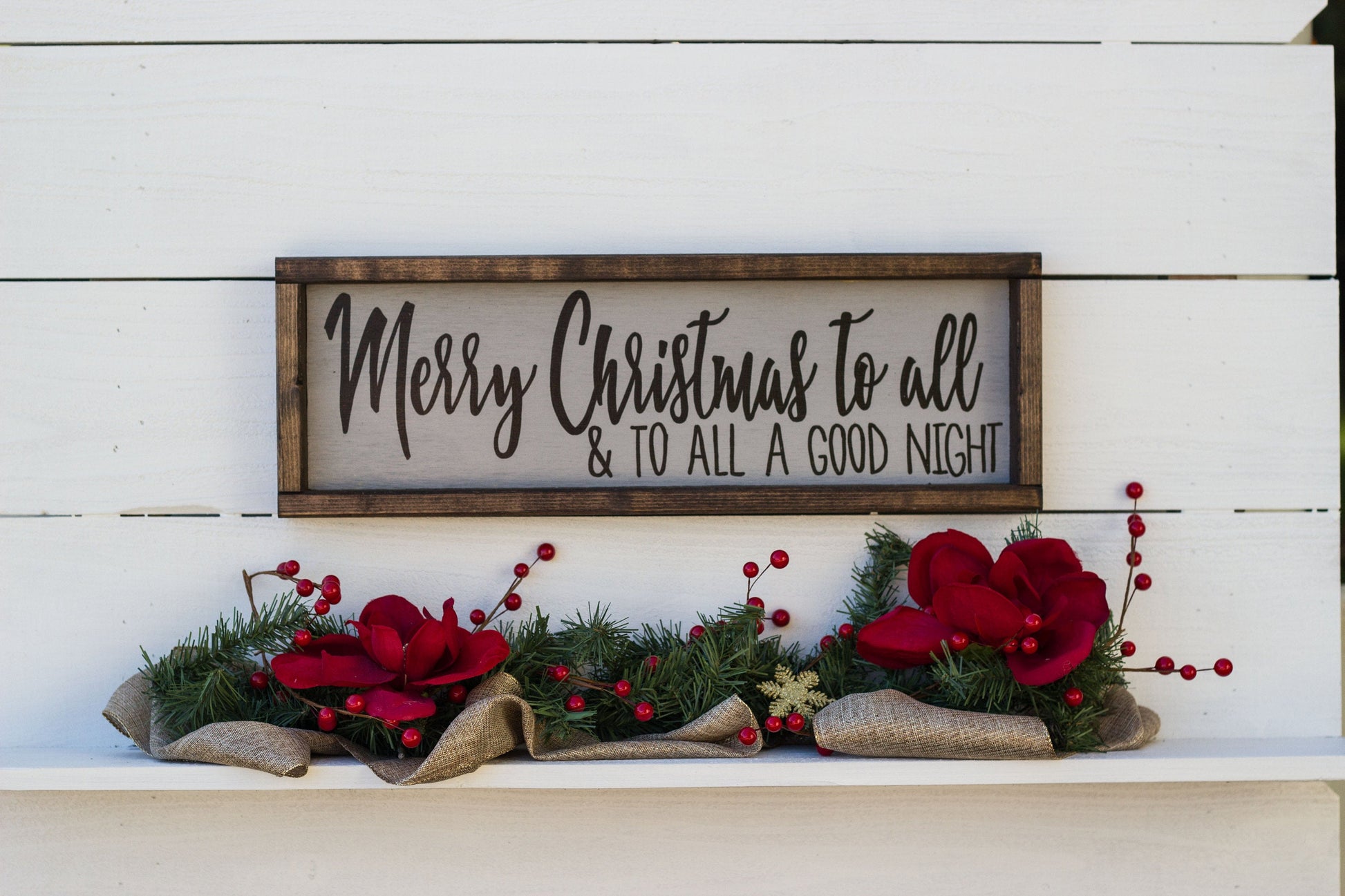 Decorative sign with 'Merry Christmas to all & to all a good night' text, surrounded by festive decorations on a white wooden background.