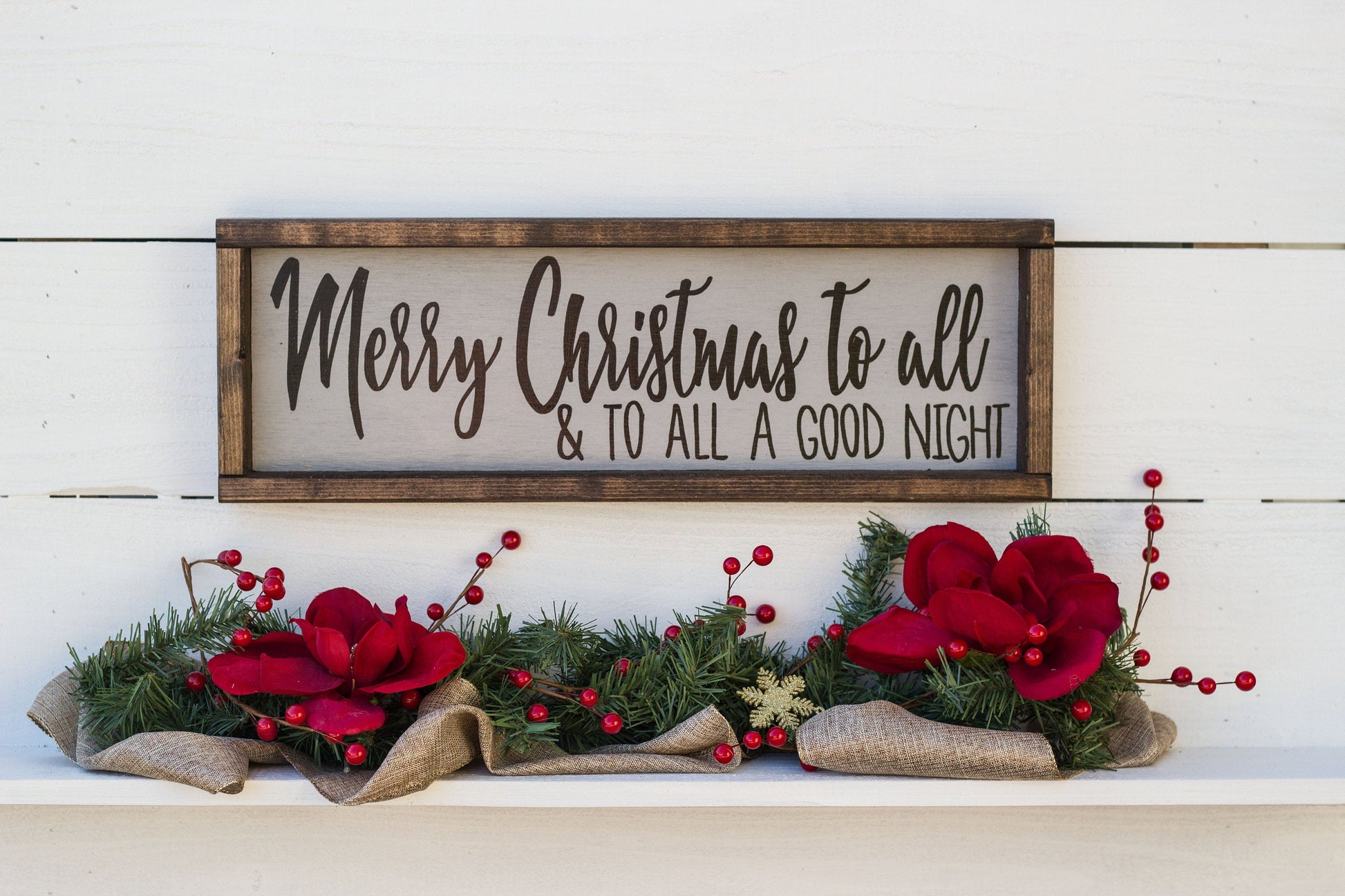 Decorative sign with 'Merry Christmas to all & to all a good night' text, surrounded by festive flowers and greenery on a white wooden surface.