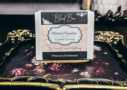 Witch's Familiar Crystal Carving blind box on a decorative surface with plants in the background