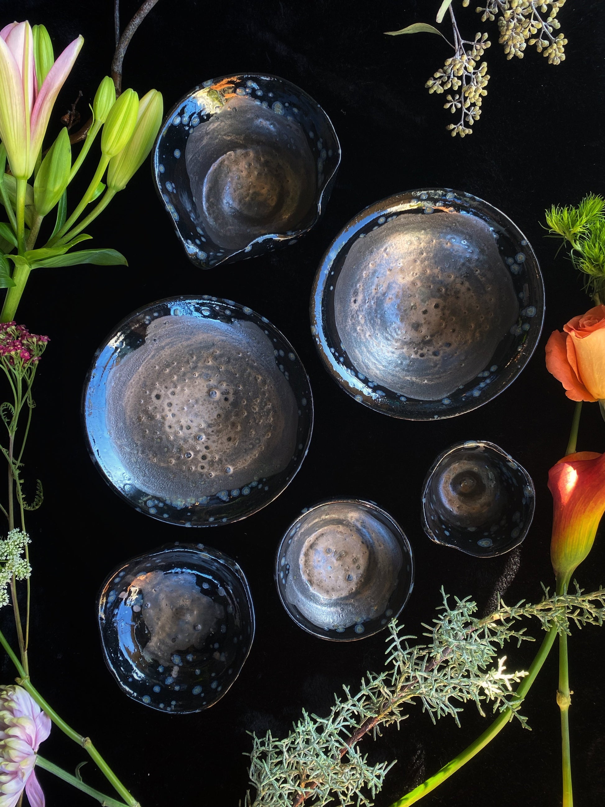 Set of black ceramic bowls on a dark surface with flowers around