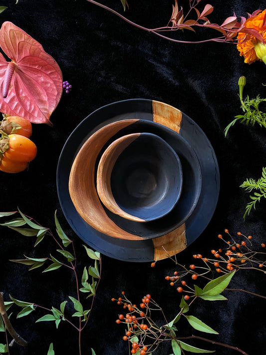 Set of three ceramic bowls with wooden accents on a dark background with decorative plants and flowers.