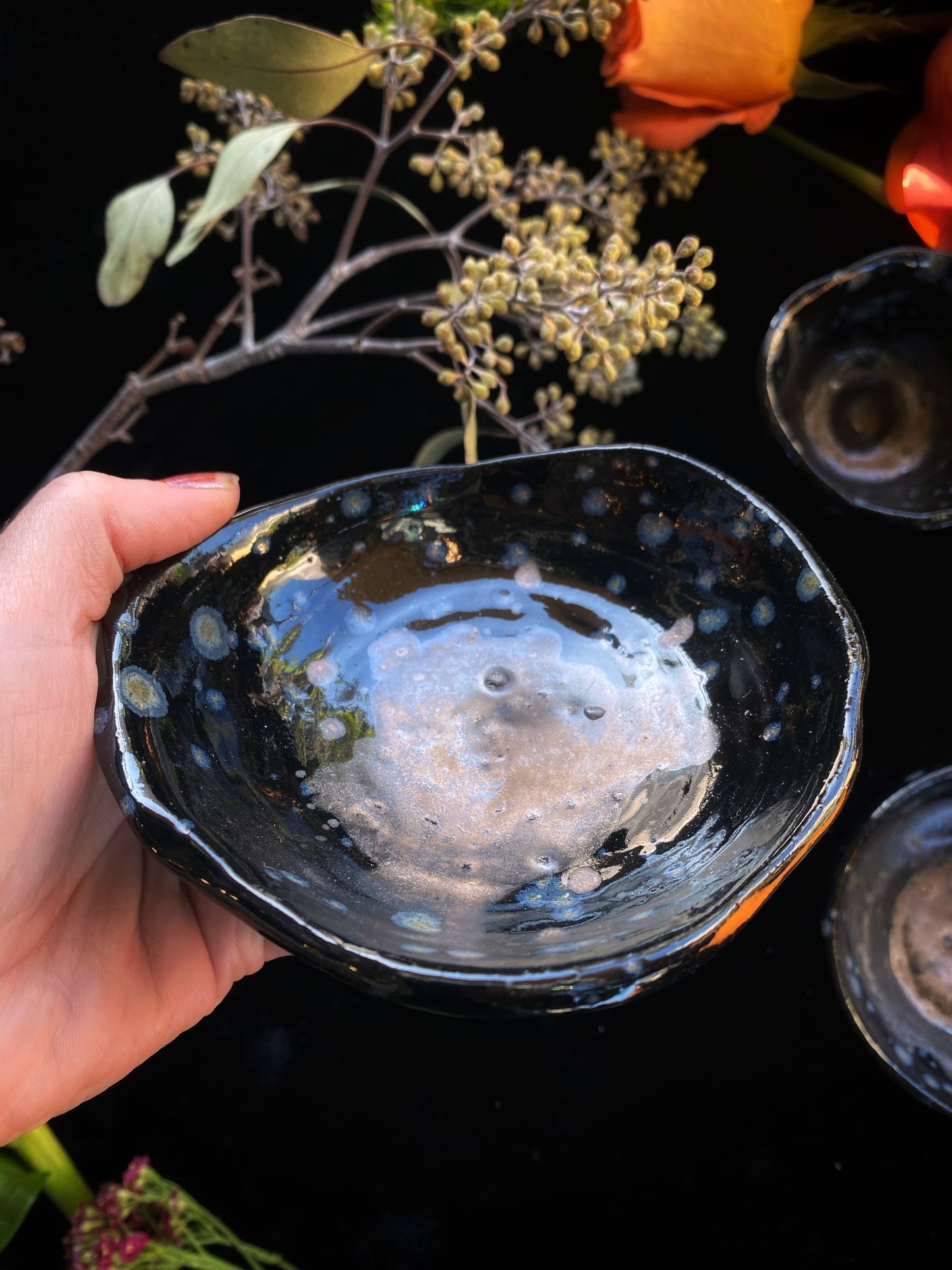 Hand holding a black ceramic bowl with white interior against a dark background