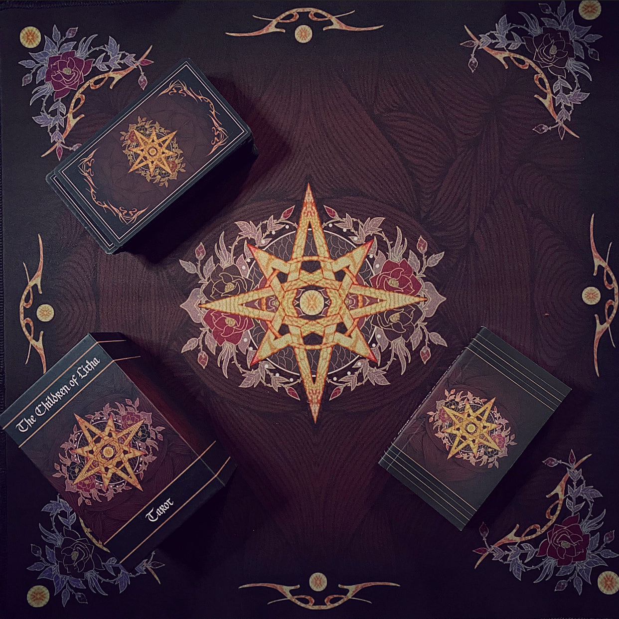 Three boxed card decks arranged on a dark patterned surface with a large ornate star emblem in the center. The boxes are black with gold and burgundy decorative graphics and visible text including 'The Chosen of Club' and 'Cares'.