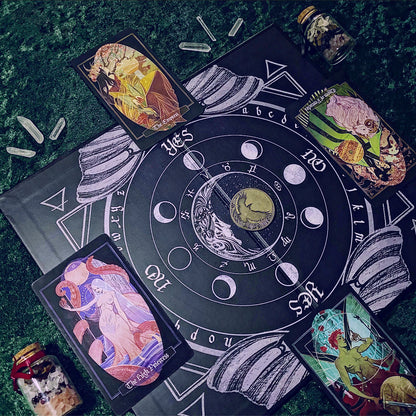 A tarot card deck and matching ritual mat laid out on a dark green textured surface. The central black circular mat features white moon phases, zodiac symbols, and a central moon illustration, surrounded by four illustrated tarot cards and small glass jars.