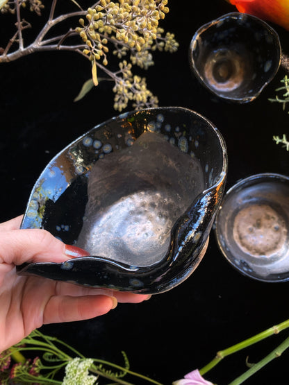 Hand holding a black ceramic bowl with a textured interior against a dark background
