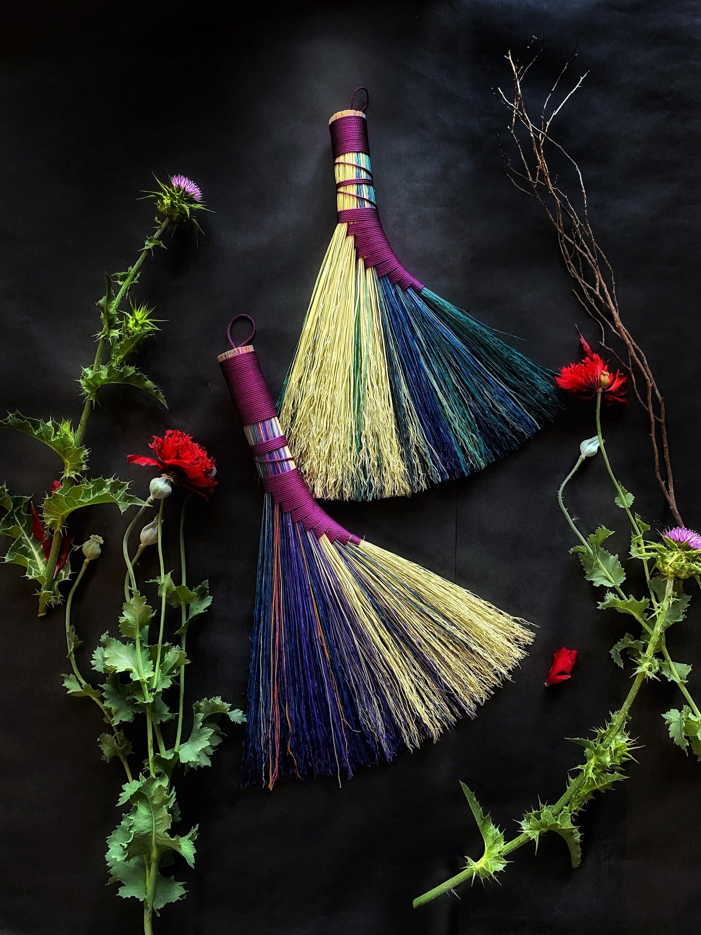 Colorful broom with purple handle and bristles on a dark background with green plants and red flowers.